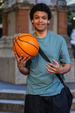 African american man holding basketball and smiling on urban steps wearing crossbody bag