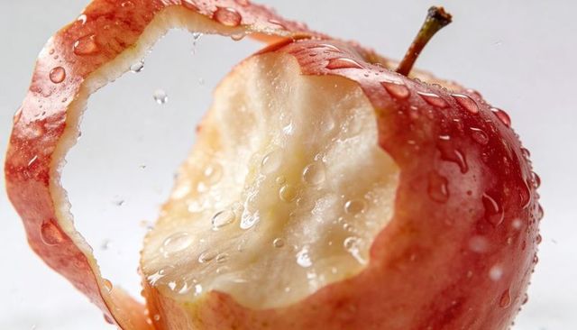 Crisp red apple glistening with water droplets and spiral peel curling after bite