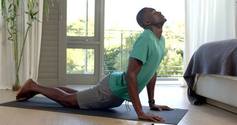 African American man practicing yoga backbend on mat in sunlit bedroom with balcony view