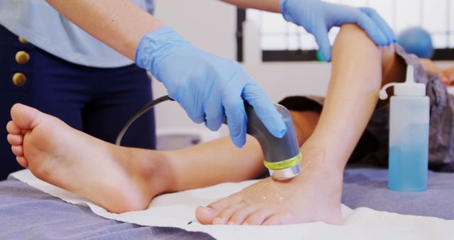 A physical therapist in blue gloves is applying ultrasound therapy on the foot of a young patient lying on a treatment table. This image is ideal for use in healthcare websites, medical blogs, physiotherapy brochures, and educational materials on rehabilitation and physical treatment methods.