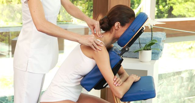 A female massage therapist is working on a young Caucasian woman's back, with copy space. They are in a serene setting that suggests a spa or wellness center, emphasizing relaxation and therapeutic touch.