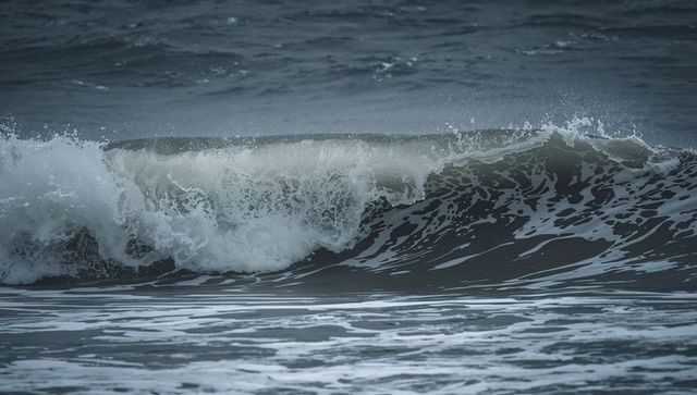 Moody ocean wave crashing at shoreline with foamy white surf and spray