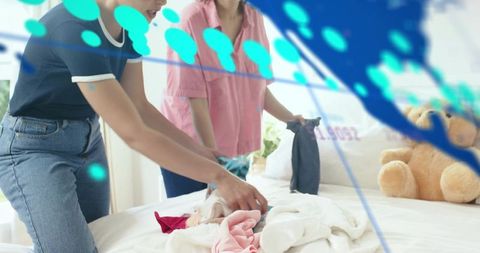 Collaborating on closet declutter: women folding clothes on sunlit bed with teddy bear