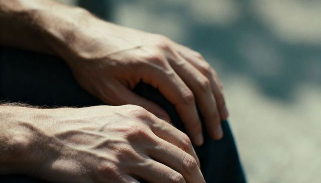 Resting male hands showing prominent veins and knuckles on denim lap closeup