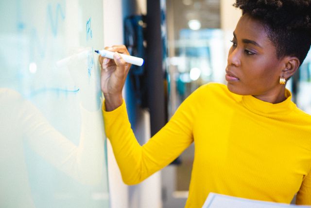 African american young businesswoman writing on whiteboard while working in office. unaltered, business, corporate business, occupation and office concept.