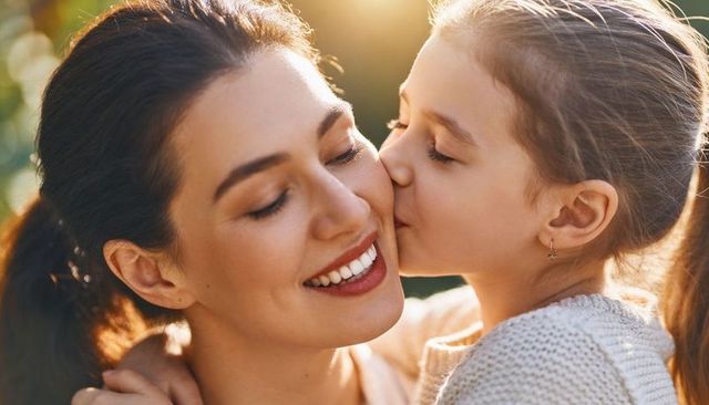 Mother and daughter sharing tender cheek kiss during golden hour embrace