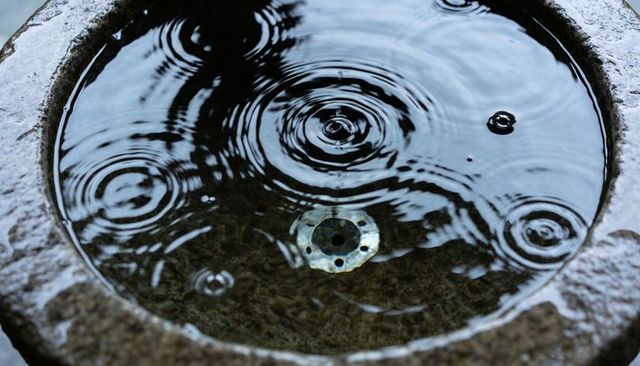 Stone basin ripples creating concentric water rings in reflective fountain with metallic drain