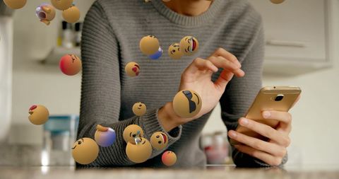 Emojis floating around woman using smartphone in kitchen