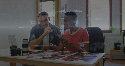 Creative duo reviewing printed layouts and tablet in daylight studio with camera gear