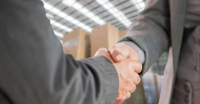 Close-up of two businesspeople shaking hands in a warehouse. Suitable for themes involving business agreements, partnerships, teamwork, logistics, and successful business transactions. Ideal for use in business-related content, presentations, and websites focusing on professional relationships and warehousing operations.