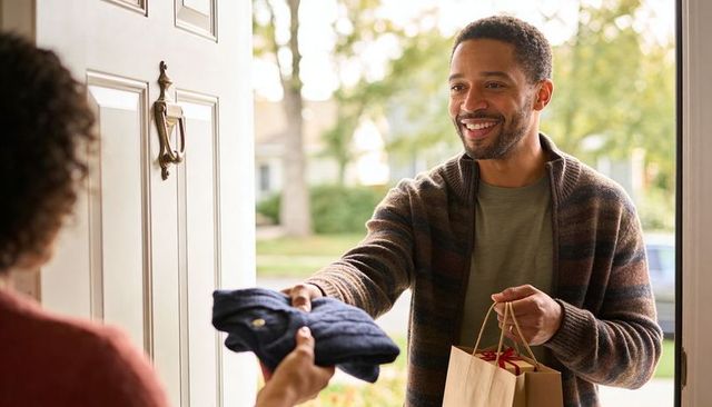 Smiling neighbor handing gift and sweater at front door, friendly porch exchange