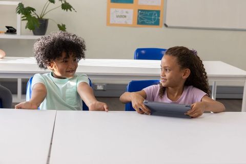 Two students sharing tablet at front row classroom desk showing collaboration and focus