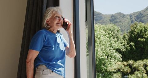 Senior Woman Enjoying Smartphone Conversation by Sunny Window