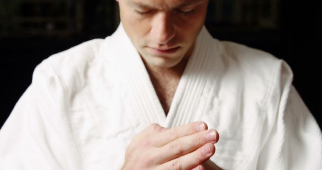 Martial artist in traditional gi practicing zen meditation while standing in a focused state. Ideal for use in topics related to martial arts, mindfulness practices, mental focus, meditation techniques, and Japanese traditional culture. Suitable for fitness and wellness blogs, training guides, self-improvement articles, and promotional materials for martial arts schools.