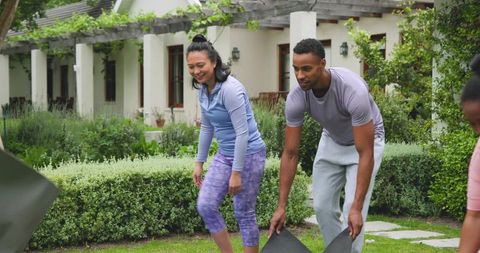 Diverse friends rolling out outdoor workout mats on suburban lawn for group fitness