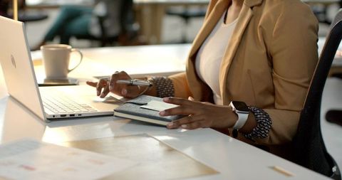 African American Businesswoman Working at Desk with Laptop and Planner in Sunlit Office