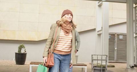 Mature couple strolling urban plaza with woman carrying green tote and knit beanie
