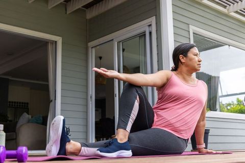 Mature woman practicing seated spinal twist on porch yoga mat for outdoor wellness