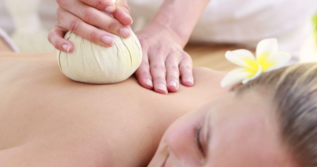 This image captures a person receiving a traditional Thai herbal compress massage. Seen on their back, a therapist uses herb-filled pouches for therapeutic benefits. Perfect for promoting spa services, wellness retreats, and holistic healing practices. Emphasizes relaxation and self-care.