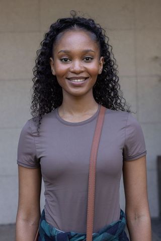 Confident young woman smiling in mauve top with crossbody bag, urban minimalist portrait