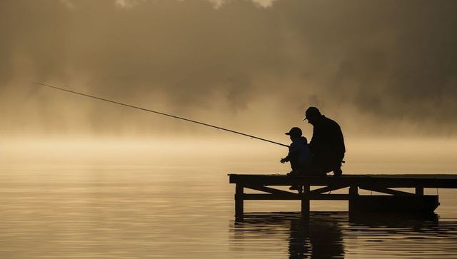 Father and son fishing on misty lakeside pier at dawn