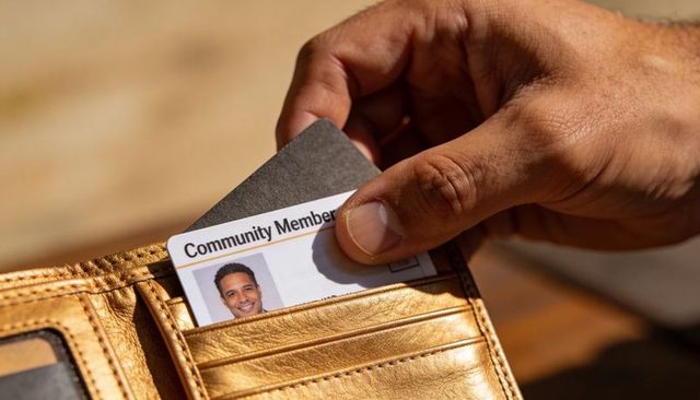 Hand placing community membership card into tan leather wallet closeup in warm sunlight