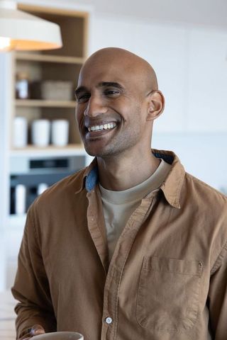African american man smiling while holding ceramic mug in modern minimalist kitchen