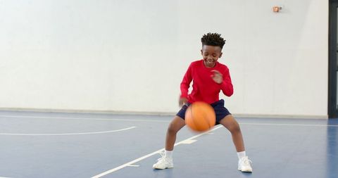 African American Boy Dribbling Basketball on Indoor Gym Court Smiling and Practicing