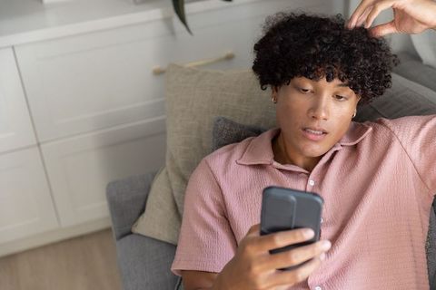 Young man reclining on sofa checking smartphone during relaxed home downtime, casual lifestyle
