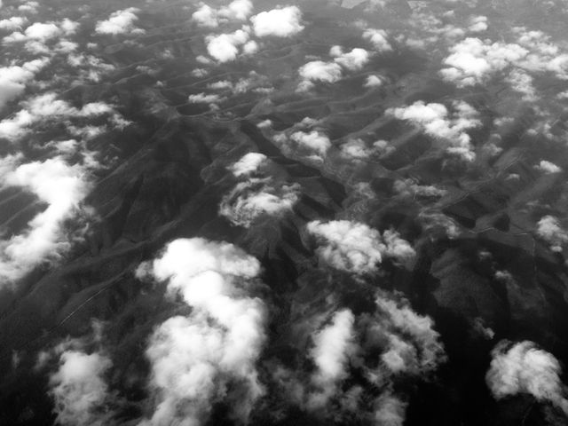 Aerial view showing clouds scattered over a mountainous landscape in monochrome. Useful for travel blogs, nature documentaries, environmental awareness campaigns, and artistic projects seeking to emphasize natural beauty or atmospheric conditions.