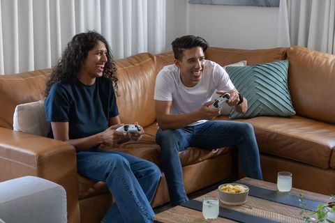 African american couple laughing and playing video games on sectional sofa in living room
