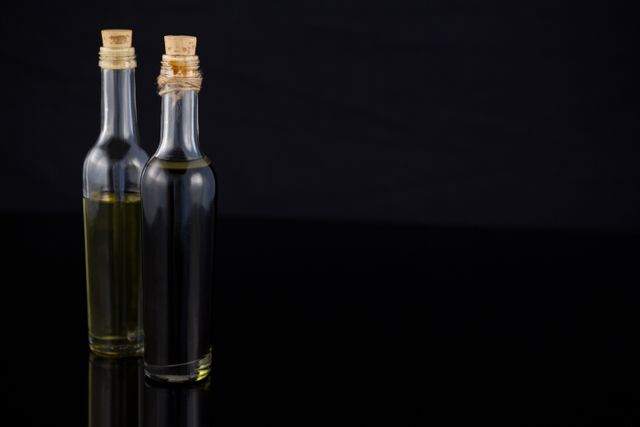 This image showcases a close-up view of olive oil and balsamic vinegar bottles with cork stoppers against a black background. Ideal for use in culinary blogs, cooking websites, gourmet food promotions, and kitchen-related advertisements. The dark background and reflective surface add a touch of elegance, making it suitable for high-end food and beverage marketing materials.