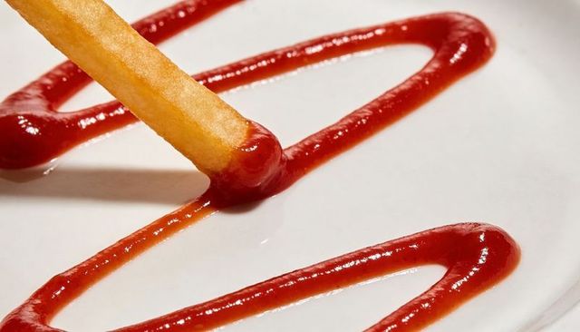Crispy french fry dipping into ketchup zigzag on white plate closeup macro food