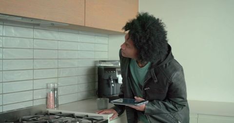 African american man inspecting kitchen cabinet while using tablet near gas cooktop