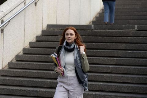 Red-haired student walking down city stairs holding colorful notebooks and backpack