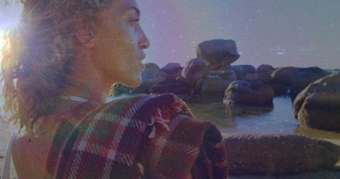 Woman reflecting on rocky shoreline during sunset