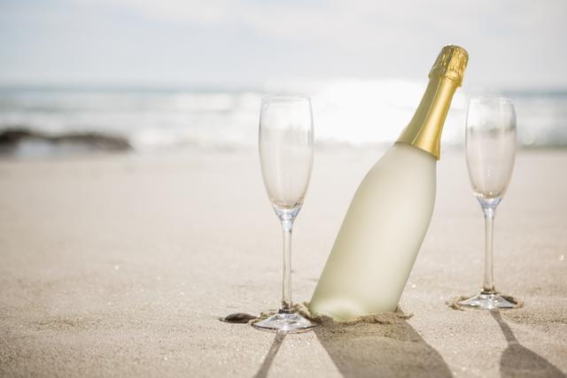 Champagne bottle and two glasses on sand at tropical beach