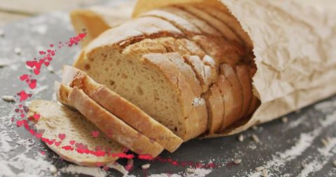 Rustic sliced artisan bread in paper bag with flour dusting and pink heart overlay