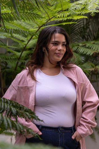 Young woman standing among ferns wearing pink overshirt and jeans, serene garden portrait