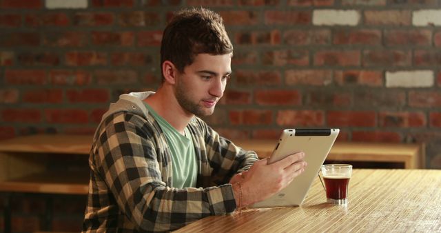 Young man sitting in cafe browsing tablet, drinking coffee. Ideal for ads about digital devices, leisure time, or cafes