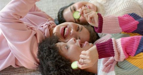 Sharing laughs and cucumber spa moments: diverse friends relaxing on sofa in knitwear