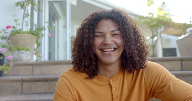 Portrait of happy biracial man with long curly hair smiling in sunny garden. Summer, nature, domestic life and lifestyle, unaltered.