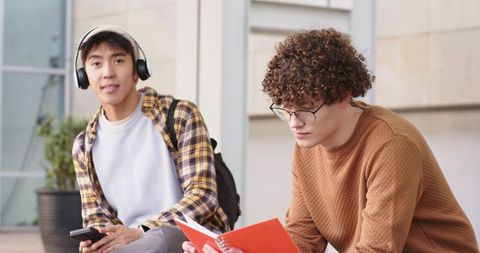 Diverse male students studying outdoors on campus with headphones and notebook