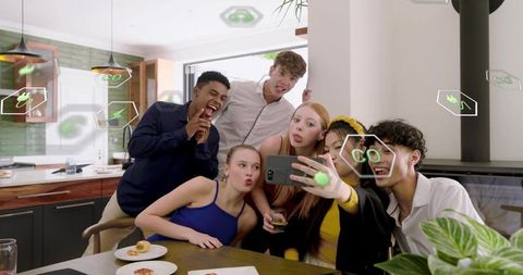 Group of young friends taking smartphone selfie with holographic ar icons in modern kitchen