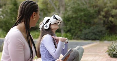 Woman trying vr headset with friend while holding tablet in outdoor courtyard