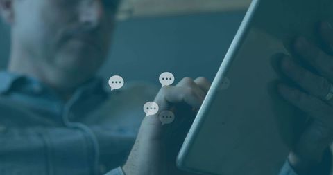 Man using tablet messaging app with floating chat bubbles in casual home interior