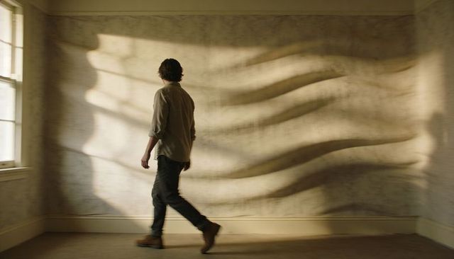 Man walking past rippled shadow waves on textured wall in sunlit minimalist interior