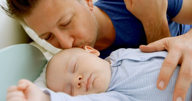 A Caucasian man gently kisses his sleeping baby, with copy space. It's a tender moment capturing the affectionate bond between a father and his child.