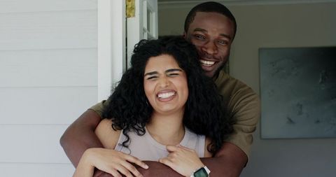 Diverse couple hugging and laughing at home entryway with smartwatch visible, warm moment