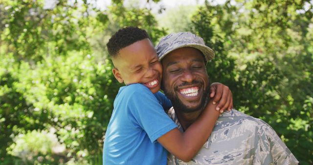 Happy african american soldier father and son embracing and smiling in garden. Military service, fatherhood, family and togetherness.